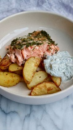 a white plate topped with potato wedges next to a bowl of dip and salmon