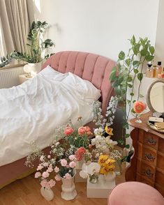 a bed with white sheets and pink tufted headboard next to vases filled with flowers