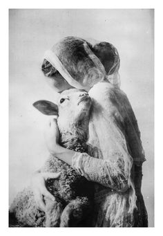 an old black and white photo of a woman holding a lamb in her arms,