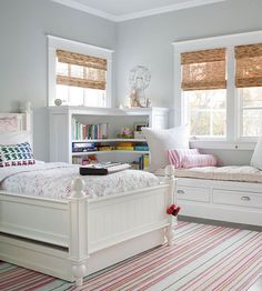 a bedroom with white furniture and striped rugs in front of two windows that have roman shades on them