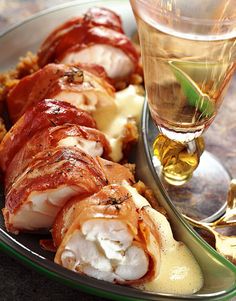 a plate with bacon wrapped in cheese next to a glass of wine