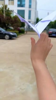 a hand holding an origami airplane in front of a parking lot