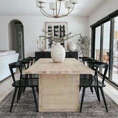 a dining room table with black chairs and a vase on top of it in front of an open glass door