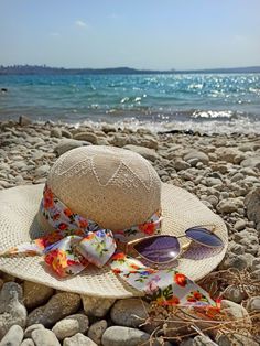 a hat and sunglasses on the beach with water in the backgroung behind it