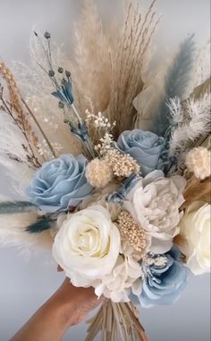a person holding a bouquet of flowers in their hand with feathers on the bottom and blue, white and beige colors