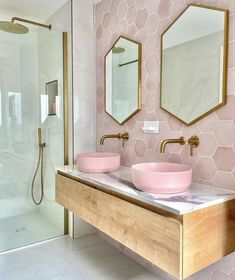 two pink bowls are on the counter in this bathroom with hexagonal tiles and gold fixtures