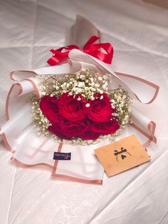 a bouquet of red roses and baby's breath wrapped in white paper on a bed