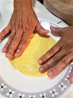 two hands that are touching each other on a white and gray plate with yellow dough