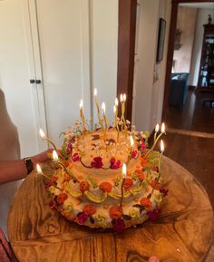 a birthday cake with many lit candles on the top and flowers all over it, sitting on a table in front of a door