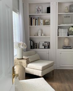 a living room filled with white furniture and bookshelves next to a window on top of a hard wood floor
