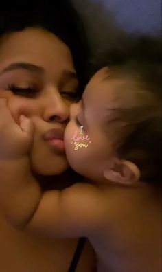 a woman kissing a baby with the words love you written on her cheek in white