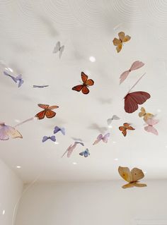 many butterflies are flying in the air above a white room with a light fixture on the ceiling