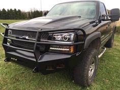 the front end of a black truck parked on top of a grass covered field with trees in the background