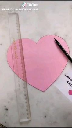a pink heart cut out from a piece of paper next to a pencil and ruler