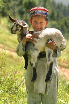 a young boy holding a baby goat in his arms