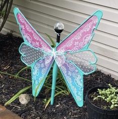 a butterfly statue sitting on top of a flower pot next to a plant in front of a house
