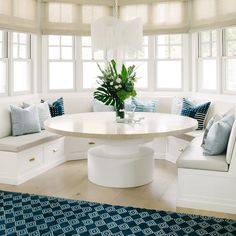 a white table with blue and white pillows on it in front of two large windows
