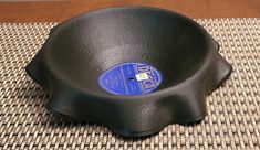 an empty black bowl sitting on top of a mat with a wooden table in the background