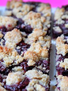 blueberry crumb bars cut into squares on a white plate with pink and purple background