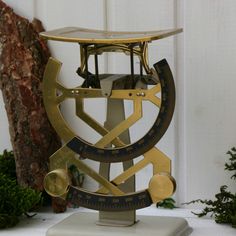 an antique brass and black clock sitting on top of a white table next to a tree