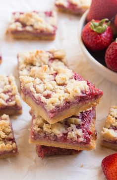 strawberry crumb bars are stacked on top of each other next to a bowl of strawberries