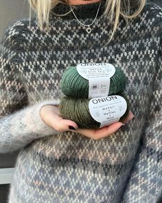 a woman holding two skeins of yarn in her hands, one green and the other grey