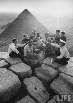 a group of men sitting on top of a rock formation with the pyramid in the background