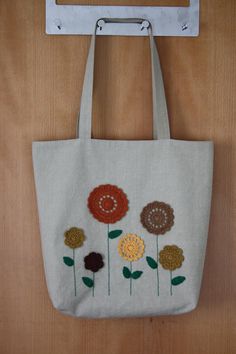 a white bag with flowers embroidered on it hanging from a metal hook, against a wooden wall