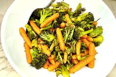 a white bowl filled with broccoli and carrots on top of a table