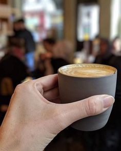 a hand holding a cup of coffee in front of a group of people sitting at tables