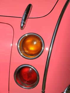 the front end of an old pink car with its lights turned on and taillights showing