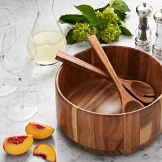 a wooden bowl with spoons in it next to some sliced peaches and wine glasses