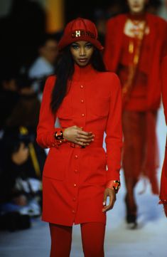 a model walks down the runway wearing red clothes and matching accessories with other people in background