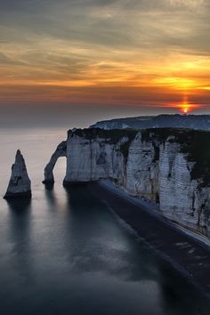 the sun is setting over the ocean and cliffs in the water, along with an arch shaped rock formation