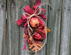 an autumn wreath with pomegranates and leaves hanging on a wooden fence