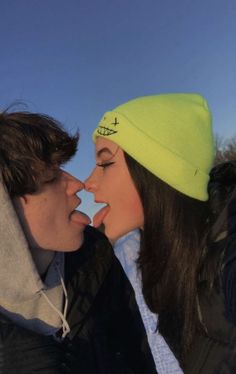 a man and woman kissing each other while wearing winter hats on top of their heads