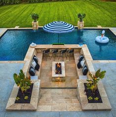 an aerial view of a pool with patio furniture and fire pit in the center surrounded by grass