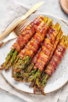 asparagus wrapped in bacon on a plate with goldware and fork next to it