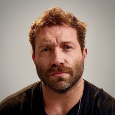 a man is looking at the camera while wearing a black t - shirt and necklace