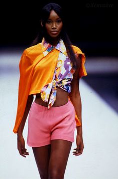 a model walks down the runway in pink shorts and an orange top with flowers on it