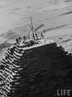 black and white photograph of people standing on top of a brick structure in the desert