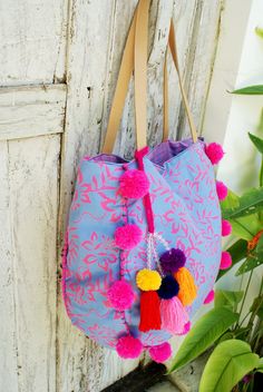 a pink and blue handbag hanging on a white wooden door with colorful pom - poms