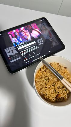the tablet is next to a bowl of noodles with chopsticks in front of it
