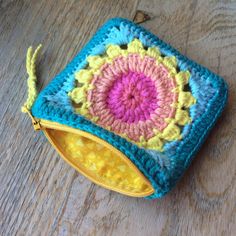 a small crocheted pouch sitting on top of a wooden table next to a yellow zipper