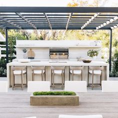 an outdoor kitchen with bar stools and white counter tops, surrounded by greenery