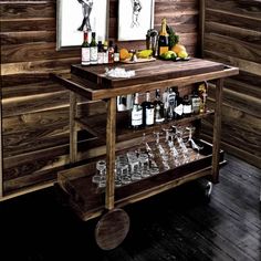a bar cart with wine glasses and bottles on it in front of two framed pictures
