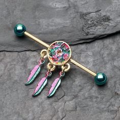 a gold barbell ring with pink and green feathers on it, sitting on top of a rock