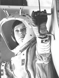 a woman in an astronaut's spacesuit looking at the camera with her hand up