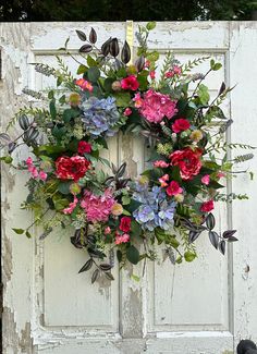 a wreath is hanging on an old door with flowers and greenery around the wreath