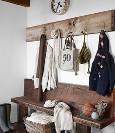 a wooden bench with several coats hanging on the wall and two clocks above it, along with other items